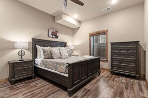 Une chambre à coucher avec un grand lit, une table de chevet, une commode et une fenêtre avec des stores.