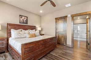 A bedroom with a wooden bed, a ceiling fan, a wooden door, and a framed picture on the wall.