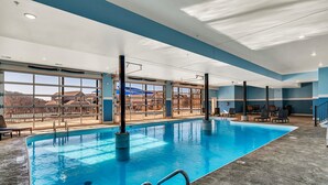 En inomhuspool med väggar av genomskinligt glas, utsikt över bergen och en modern design.