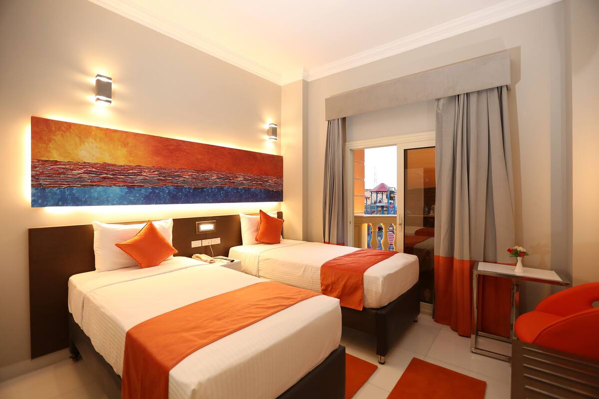 Ein Hotelzimmer mit zwei Betten, einem großen Gemälde, einem kleinen Tisch und Blick ins Freie.