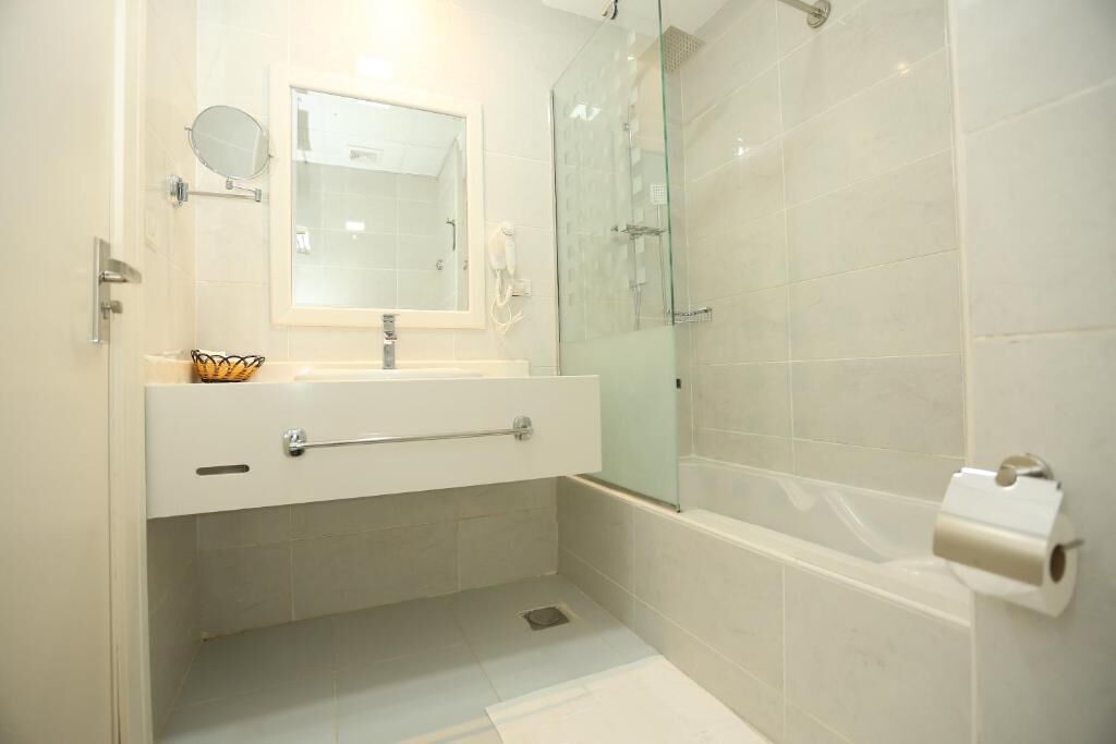 A modern bathroom with a glass shower enclosure, a white sink with a towel rack, and a toilet paper holder.