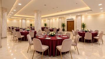 Un salón de conferencias con mesas redondas, sillas y centros de mesa con flores.
