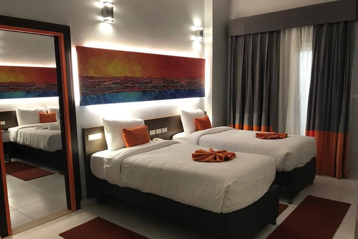 Ein Hotelzimmer mit zwei Betten, einem großen Spiegel und einem Sonnenuntergangsbild.