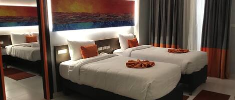 A hotel room with two beds, a large mirror, and a painting of a sunset.