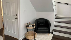 A staircase with a white railing, a black chair, a white door, and a small table with a basket and a candle. - Large, modern 2 bedroom in the heart of Forest Park (Forest Park)