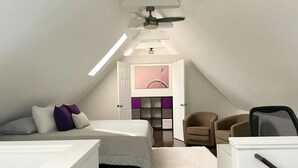 A modern, well-lit attic bedroom with a sloped ceiling, a bed with multiple pillows, a chair, a desk, and a bookshelf. - Large, modern 2 bedroom in the heart of Forest Park (Forest Park)
