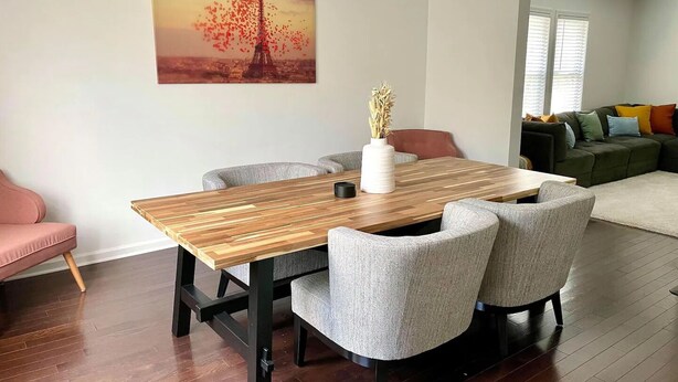 A dining area with a wooden table and four grey chairs, a vase with dried plants, and a painting of the Eiffel Tower on the wall. - Large, modern 2 bedroom in the heart of Forest Park (Forest Park)
