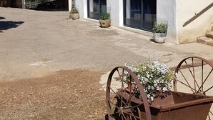 A rustic building with a tiled roof, a covered porch, and a wheelbarrow with flowers.