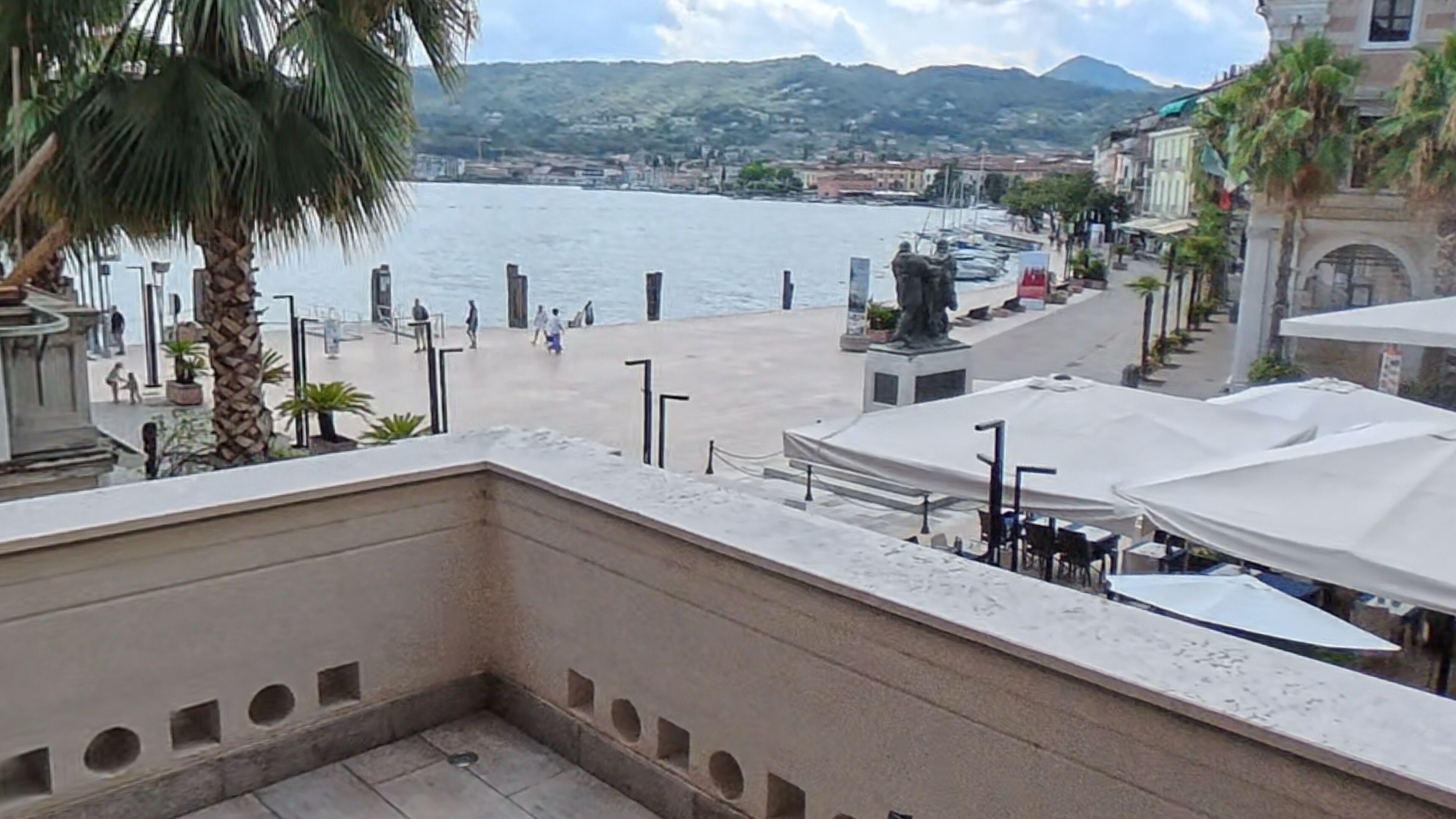 Una terraza con vista al agua, palmeras y una estatua.