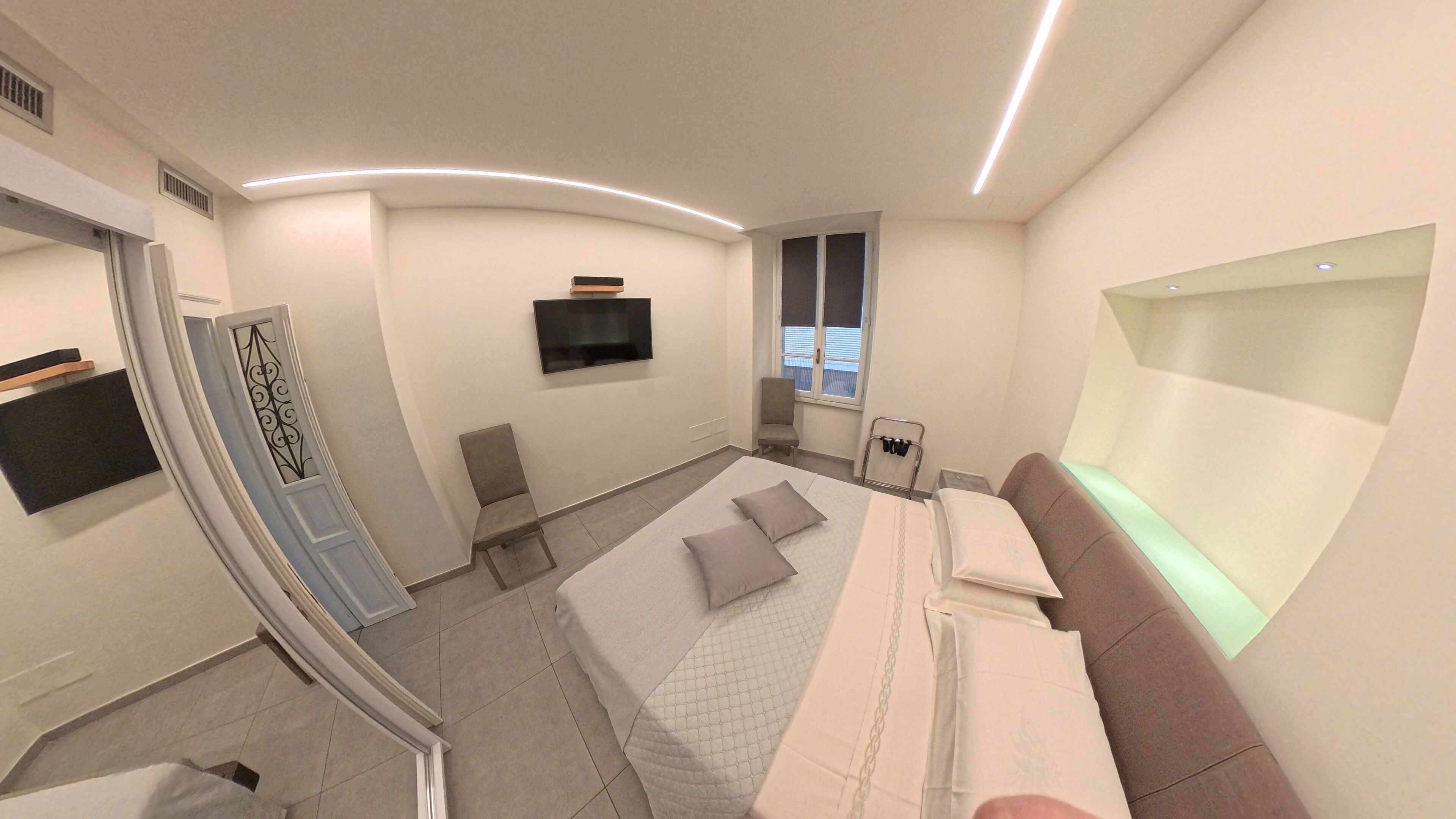 Een moderne hotelkamer met een bed, een zithoek, een aan de muur bevestigde televisie en een raam.