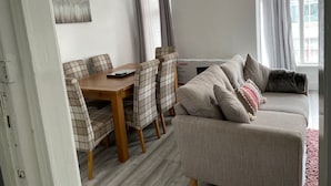 Un salon moderne avec un canapé, une table à manger et des chaises. Il y a un tableau au mur et une fenêtre avec des rideaux.