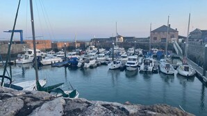 Un port de plaisance où sont amarrés de nombreux bateaux, un mur de pierre et un bâtiment sur lequel flotte un drapeau.