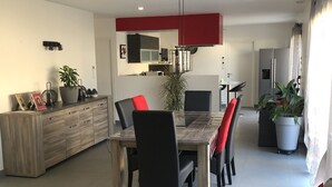 Une cuisine moderne avec un coin repas, comprenant une table en bois, des chaises noires et un mur d’accent rouge.