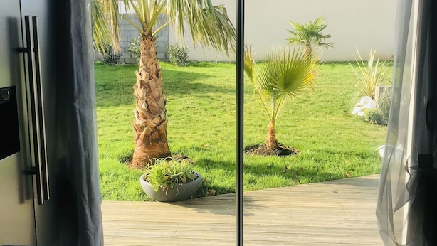 Une pièce dotée d’une porte-fenêtre coulissante qui donne sur un jardin agrémenté de palmiers et d’un petit étang.