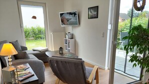 A modern living room with a sofa, a wooden rocking chair, a coffee table, and a TV mounted on the wall. - Vacation apartment for 2-3 persons on the outskirts of Wittingen (Wittingen)
