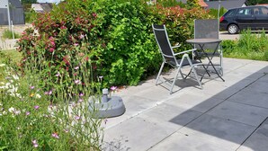 A patio with a table and chair, surrounded by lush greenery and flowering plants. - Vacation apartment for 2-3 persons on the outskirts of Wittingen (Wittingen)