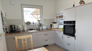 A modern kitchen with a wooden table, a coffee maker, a kettle, a microwave, and a stove. - Vacation apartment for 2-3 persons on the outskirts of Wittingen (Wittingen)