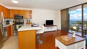 A modern kitchen with wooden cabinets, stainless steel appliances, and a dining area with a TV and balcony view.
