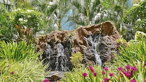 A garden with a waterfall, lush greenery, and pink flowers.