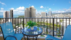 A balcony with two blue chairs, a small round table with a potted plant, and a cityscape view.