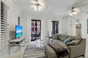 A modern living room with a sofa, coffee table, and TV. There is a balcony with a view. - Esplanade Condo | Courtyard View, Gym, Pool & Spa (Marco Island)