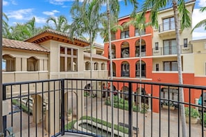 A courtyard with a pool, palm trees, and multi-story buildings with balconies.