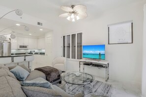 Ein modernes Wohnzimmer mit einer Couch, einem Glastisch und einem Fernseher, der eine schöne Landschaft zeigt.