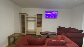 A living room with a red sofa, a wooden cabinet, and a television on the wall. - Inviting 3-bed Apartment in Stockton-on-tees (Stockton-on-Tees)