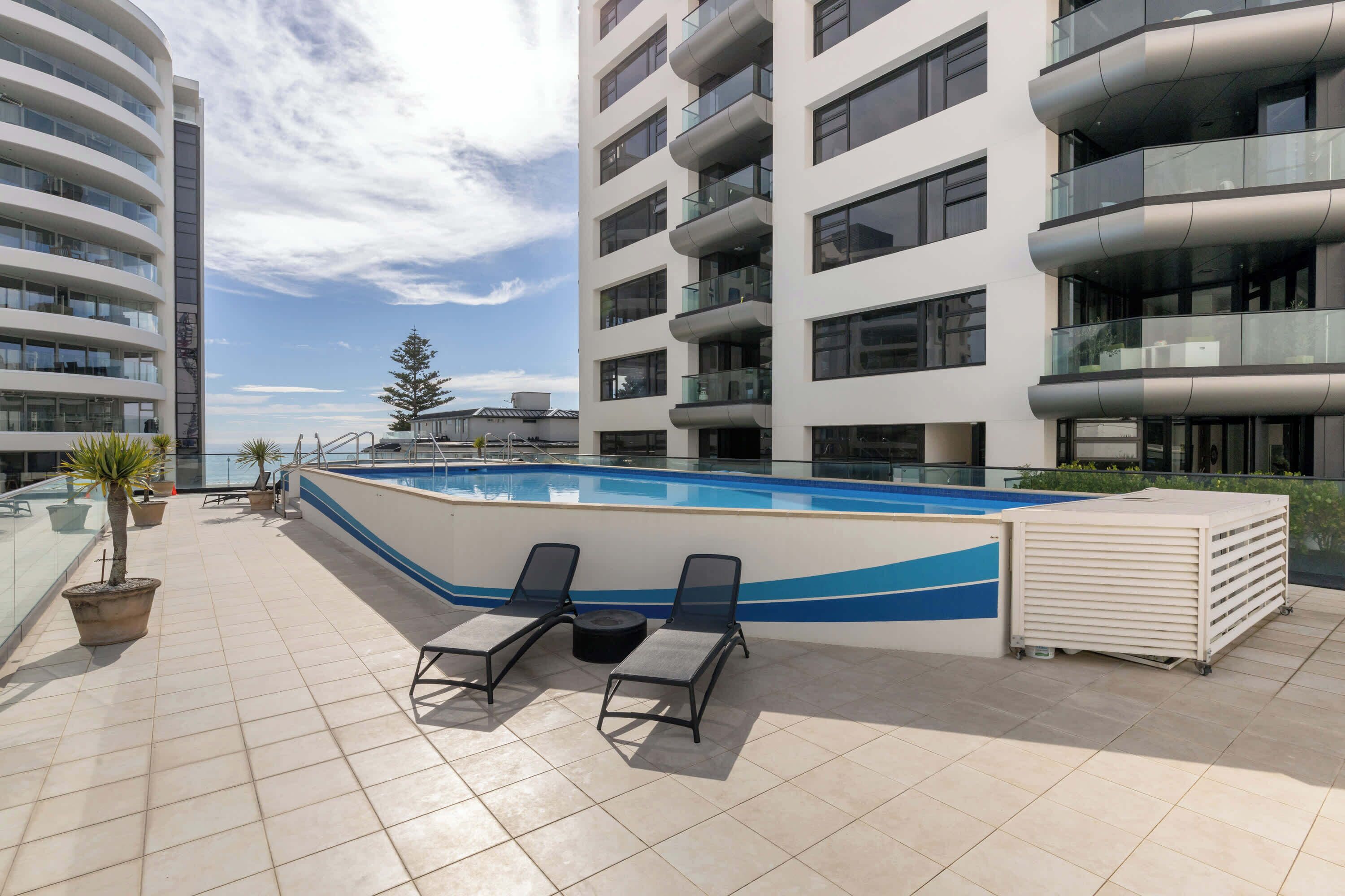 Uma área de piscina no terraço com duas espreguiçadeiras, piscina e vista para a cidade.