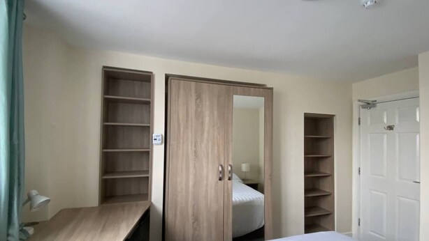 Une chambre à coucher comprenant un lit, un bureau, une armoire avec des étagères et une porte.