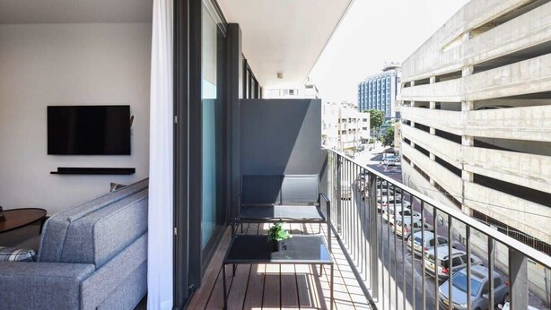 Ein Balkon mit einer Couch, einem kleinen Tisch und einem an der Wand befestigten Fernseher.