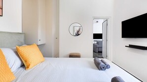Ein Hotelzimmer mit Bett, einem an der Wand befestigten Fernseher und Blick in das angrenzende Zimmer.