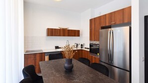 Eine moderne Küche mit Holzausstattung, einem Edelstahlkühlschrank und einem Esstisch aus Marmor mit einer Vase getrockneter Blumen.