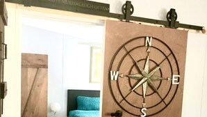 A room with a wooden floor, a bed with a teal bedspread, and a compass wall decoration.