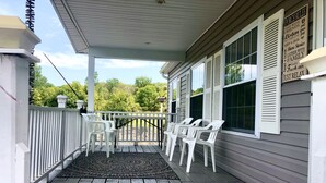 A wooden porch with white plastic chairs and a rug, overlooking a green landscape.