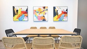 A conference room with a long table, six wicker chairs, and three abstract paintings on the wall. - Colorful 2BR next to Gazoz Beach by HolyGuest (Tel Aviv-Yafo)