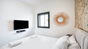 A modern hotel room with a bed, a flat-screen TV mounted on the wall, a window, and a decorative mirror. - Colorful 2BR next to Gazoz Beach by HolyGuest (Tel Aviv-Yafo)