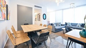 A modern living room with a wooden dining table, wicker chairs, a grey sofa, and a large window with curtains. - Colorful 2BR next to Gazoz Beach by HolyGuest (Tel Aviv-Yafo)