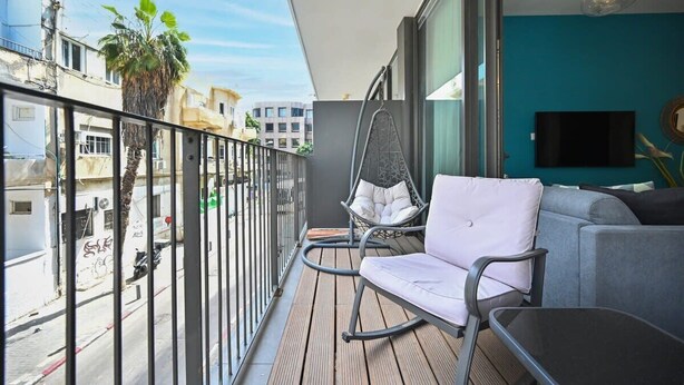 A balcony with a cushioned chair, a sofa, and a TV. - Colorful 2BR next to Gazoz Beach by HolyGuest (Tel Aviv-Yafo)