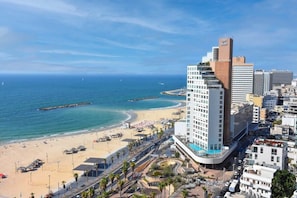 A coastal cityscape with a prominent hotel featuring a curved balcony, a beach with umbrellas, and a clear view of the ocean.