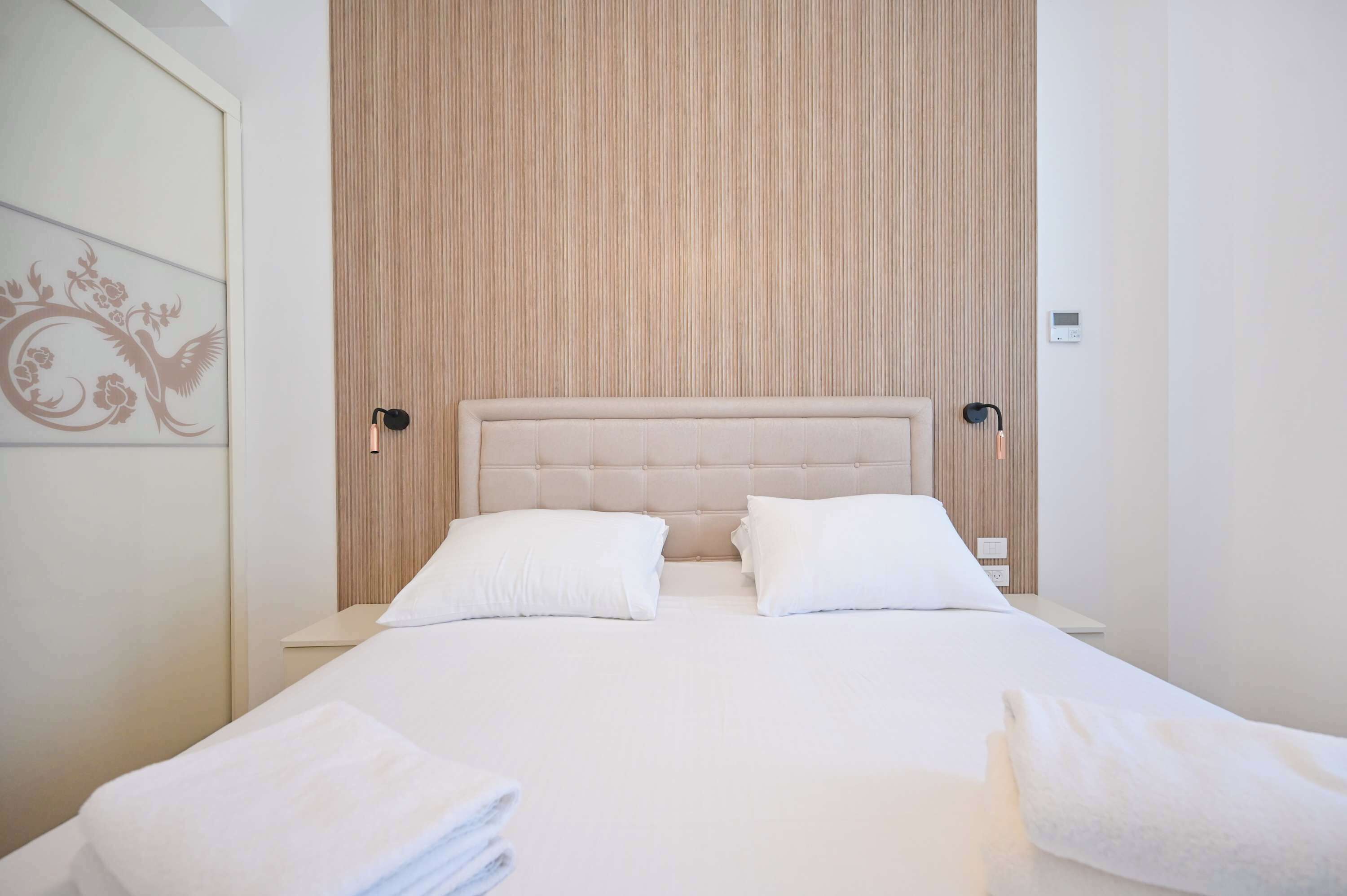 A neatly made bed with a tufted headboard, two bedside tables with lamps, and a wall with vertical wooden slats.