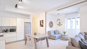 A modern kitchen with white cabinets, a dining table with chairs, a gray sofa, and a gray couch.