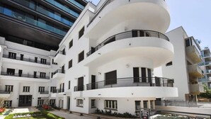 A modern multi-story residential building with balconies, a central courtyard, and a neighboring high-rise building.