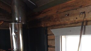 Un poêle à bois avec une cheminée, une fenêtre donnant sur des rochers et un intérieur rustique en bois.