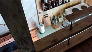 L’intérieur d’un chalet rustique en bois, avec une étagère en bois où sont rangés divers ustensiles de cuisine, un tableau encadré et une petite table avec un banc.