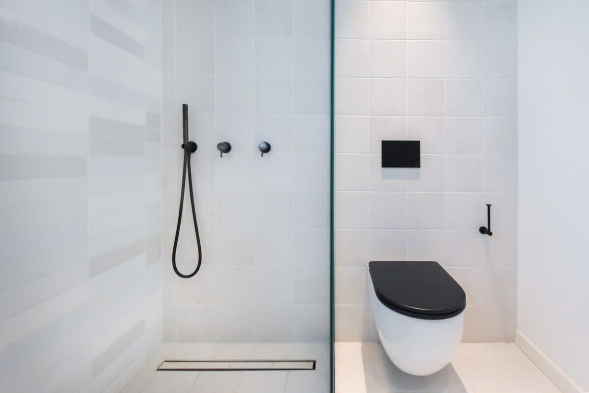 A modern bathroom with a glass shower enclosure, a white toilet, and a black sink.