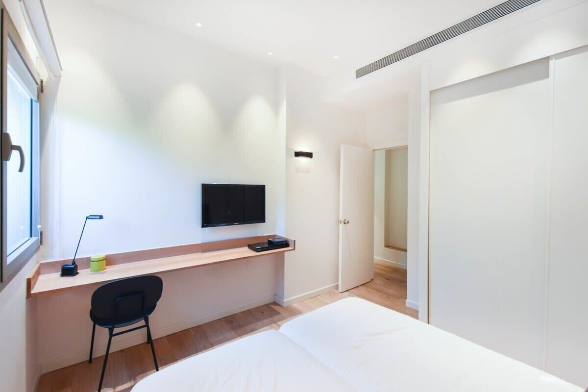 Een moderne slaapkamer met een bed, een bureau met stoel, een televisie en een kledingkast.