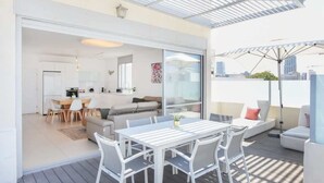 Une terrasse extérieure moderne, aménagée avec une table et des chaises, un canapé et une porte vitrée donnant sur un espace intérieur.