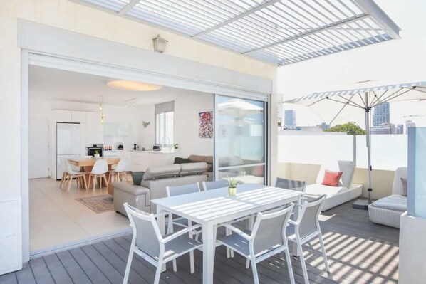 An open-plan living area with a dining table and chairs, a sofa, and a kitchen in the background.