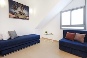 A room with two blue sofas, a small table with a plant, and a window with a view of palm trees. - 3BR Penthouse in Bograshov by HolyGuest (Tel Aviv-Yafo)